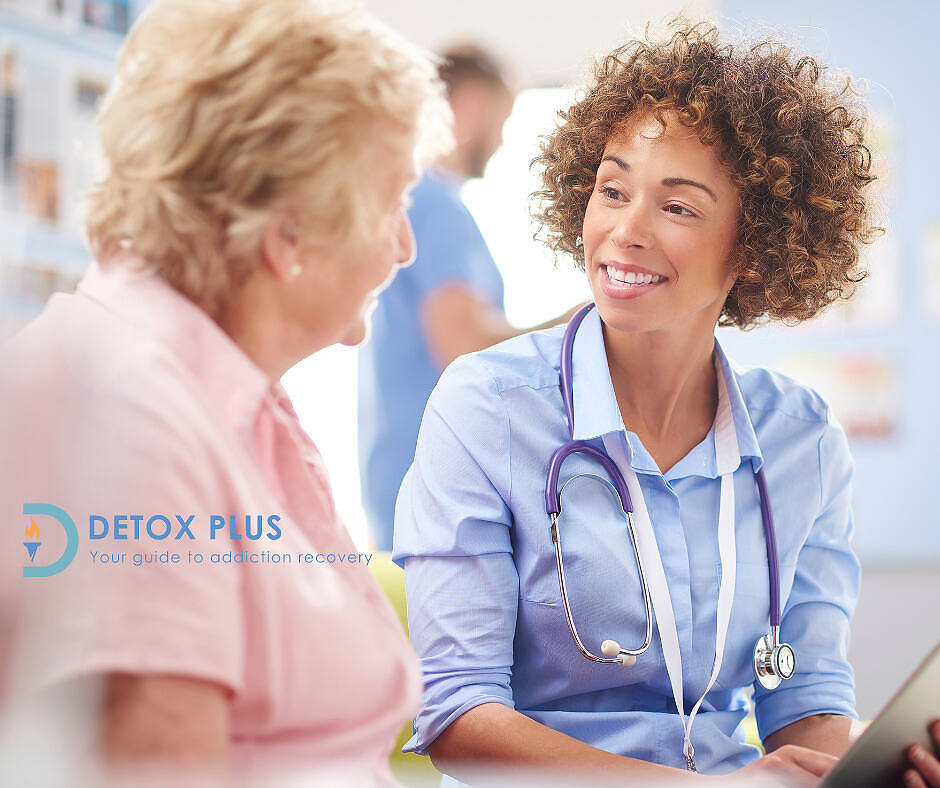 Smiling female doctor with curly hair and stethoscope consulting an older female patient in pink shirt. Detox Plus logo visible, emphasizing personalized addiction recovery guidance.