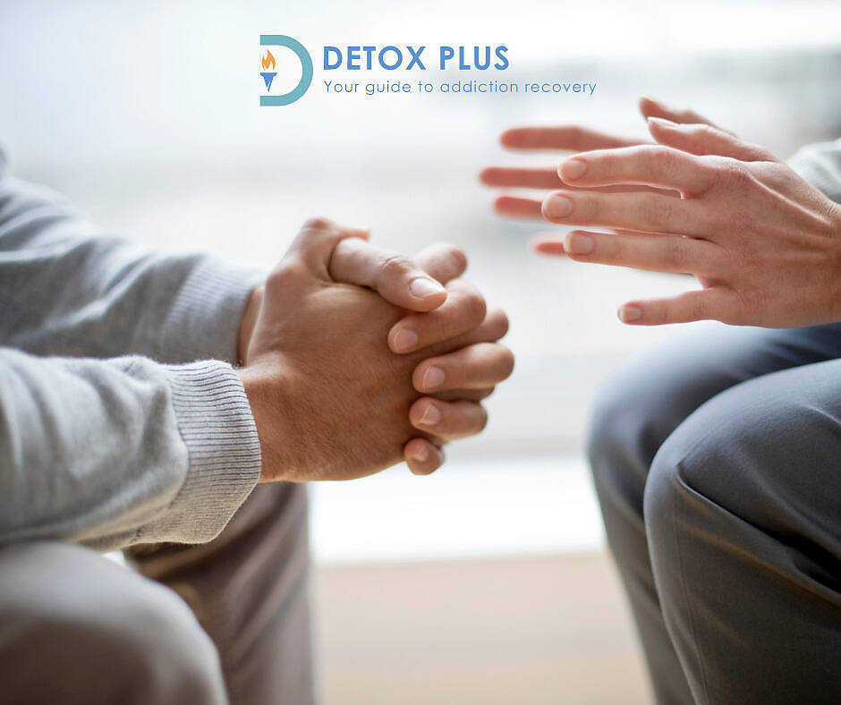 Close-up of two people's hands during a counseling session, with one person clasping their hands and the other gesturing supportively. Detox Plus UK logo and tagline "Your guide to addiction recovery" visible in the top left corner.