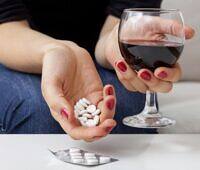 Woman's hands holding prescription pills and a glass of red wine, illustrating the dangerous combination of medication and alcohol abuse