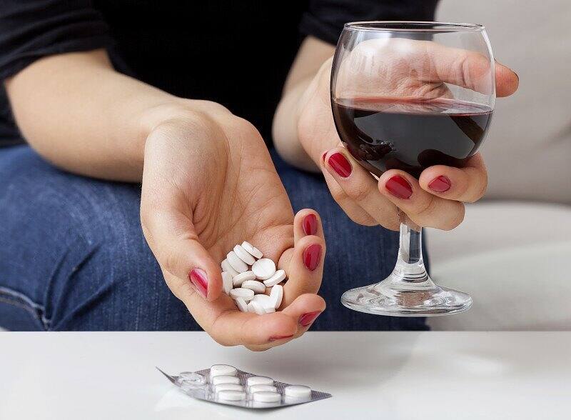 Woman's hands holding prescription pills and a glass of red wine, illustrating the dangerous combination of medication and alcohol abuse