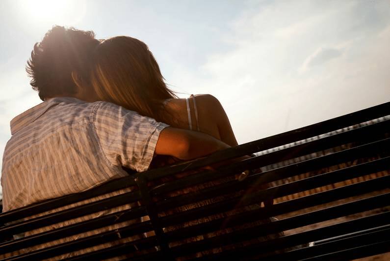 Couple embracing on a bench, backlit by sunlight, symbolizing support and companionship during addiction recovery