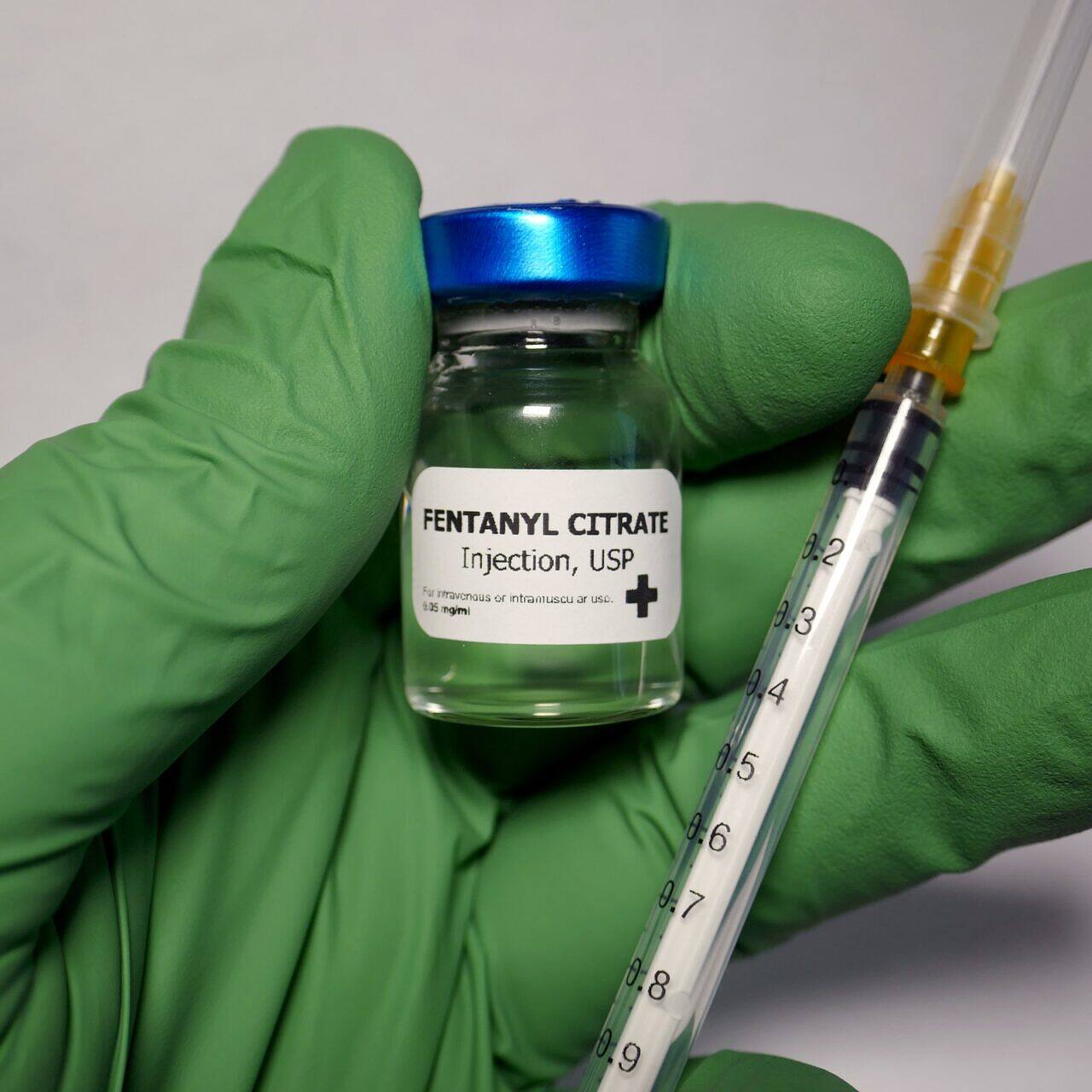 Close-up of a gloved hand holding a vial of Fentanyl Citrate injection and a syringe, highlighting the potent opioid's medical use and addiction risks