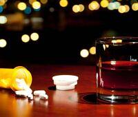 Prescription pill bottle with spilled pills next to a glass of alcohol, illustrating the dangers of combining codeine and alcohol