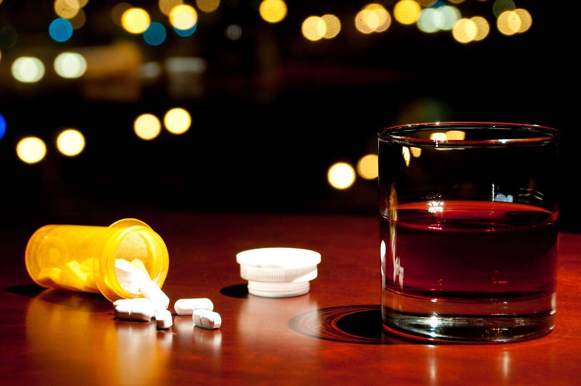 Prescription pill bottle with spilled pills next to a glass of alcohol, illustrating the dangers of combining codeine and alcohol