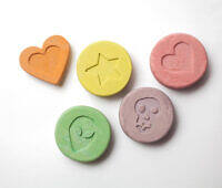 Assorted ecstasy pills in pastel colors featuring heart, star, alien, and skull designs on white background