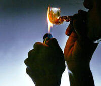 Silhouette of hands holding a lighter flame to a glass pipe, illustrating dangerous drug use and the need for addiction treatment