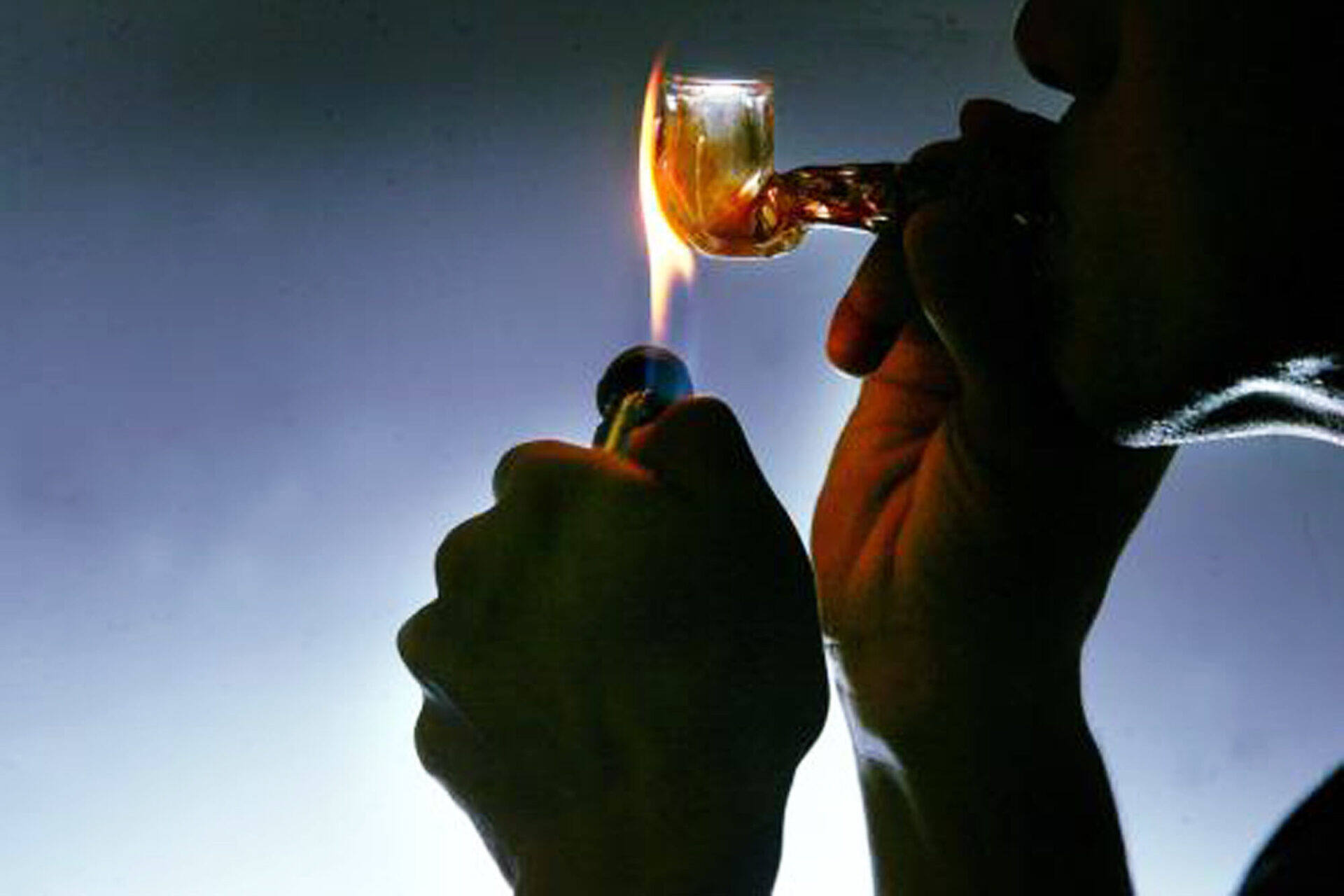 Silhouette of hands holding a lighter flame to a glass pipe, illustrating dangerous drug use and the need for addiction treatment