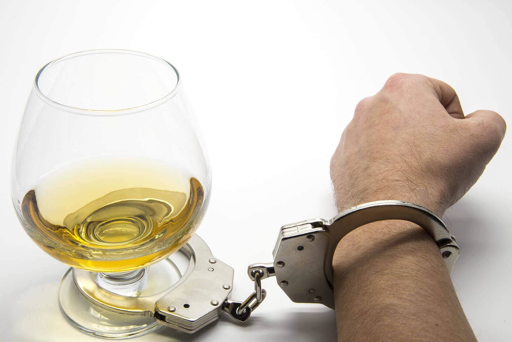 Symbolic image of alcohol addiction: a glass of whiskey connected by handcuffs to a person's wrist, representing the struggle and need for intervention in alcohol abuse