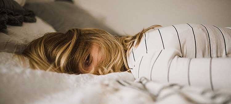 Exhausted woman with blonde hair lying face down on bed, wearing striped shirt