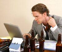 Man in suit working on laptop surrounded by beer bottles, depicting a functioning alcoholic in an office setting