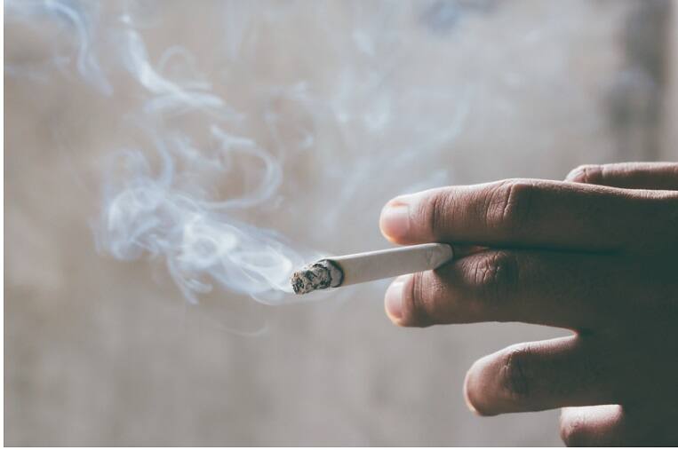 Close-up of a hand holding a lit cigarette with smoke swirling, representing nicotine addiction and substance abuse issues