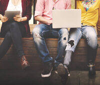 Group of diverse young adults sitting together, using tablets and smartphones, highlighting digital connectivity and potential substance abuse risks