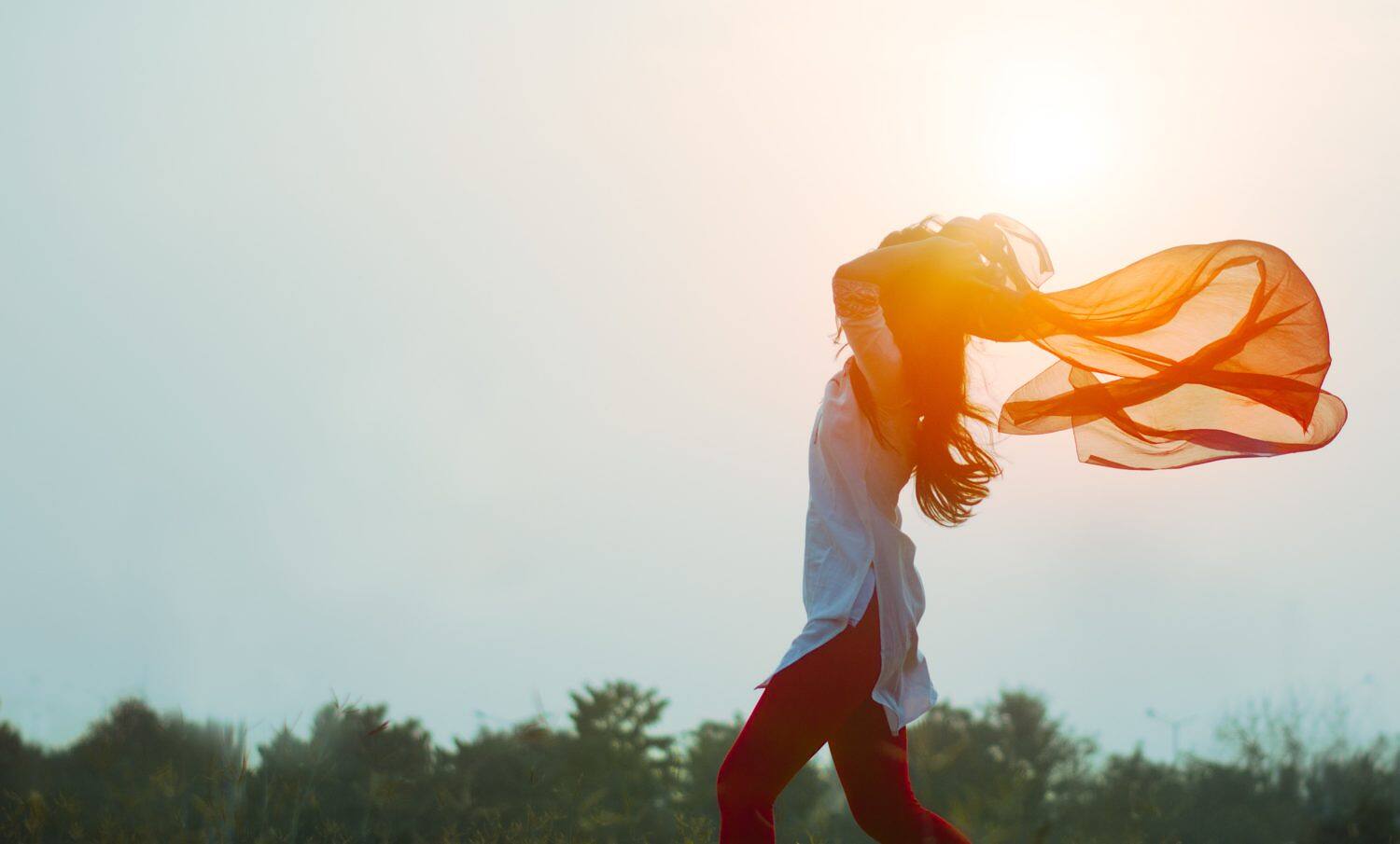 Silhouette of a woman with flowing orange scarf against sunset, symbolizing hope and freedom in addiction recovery