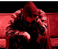 Despondent figure in red hoodie and plaid shirt sitting hunched over on a couch, symbolizing the isolation and despair often associated with substance abuse