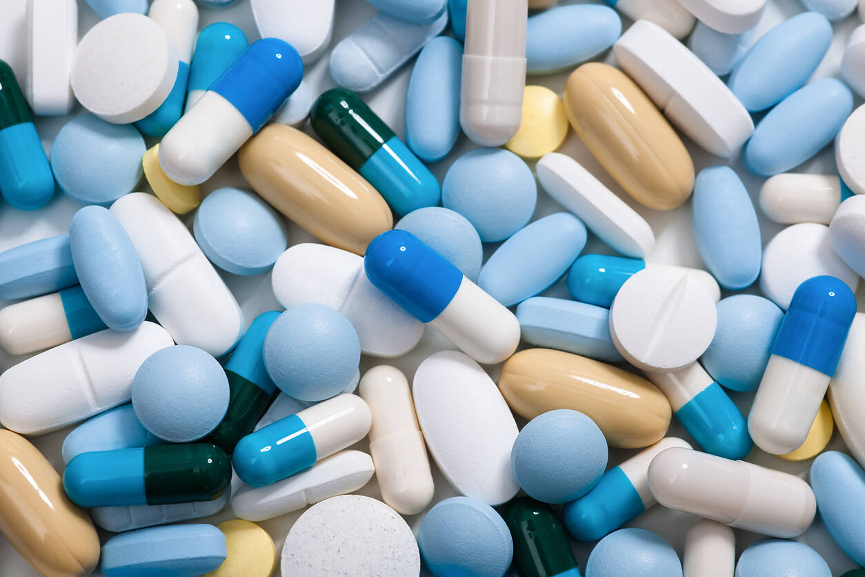 Close-up of various colorful prescription pills and capsules including blue, white, yellow, and green medications scattered together