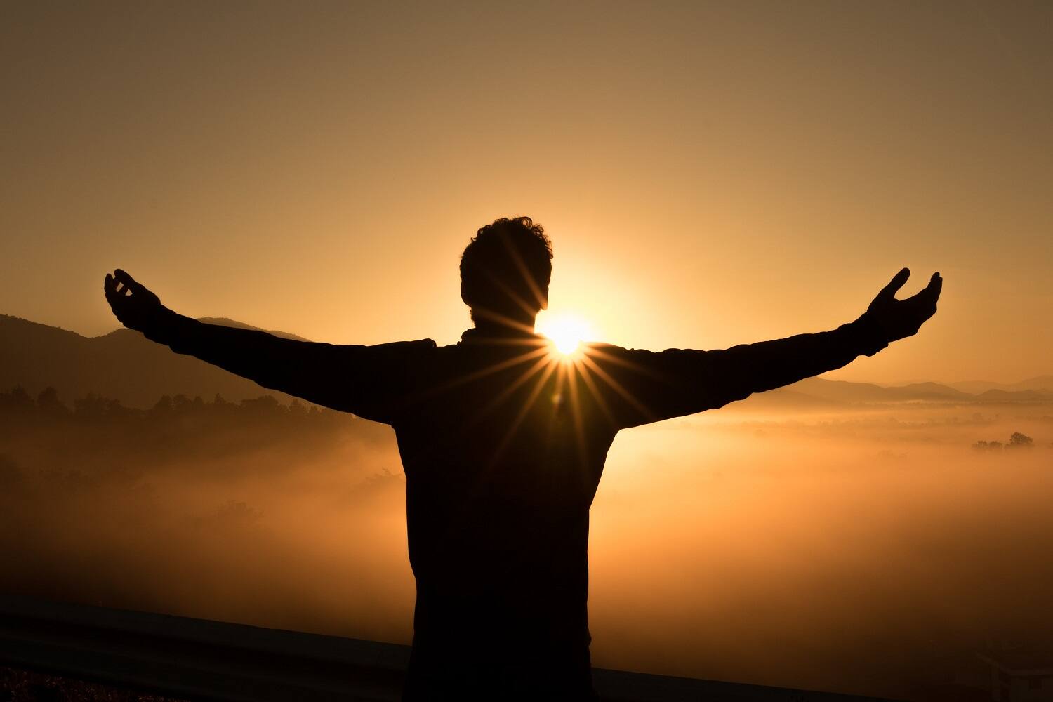 Silhouette of person with arms outstretched facing sunrise over misty landscape, symbolizing hope and new beginnings in addiction recovery