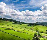 Panoramic view of Cheshire's lush green fields, stone walls, and rolling hills under a dramatic sky with fluffy clouds, offering a peaceful environment for addiction rehabilitation