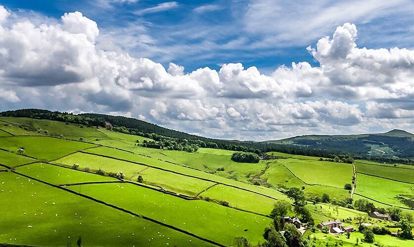 Panoramic view of Cheshire's lush green fields, stone walls, and rolling hills under a dramatic sky with fluffy clouds, offering a peaceful environment for addiction rehabilitation