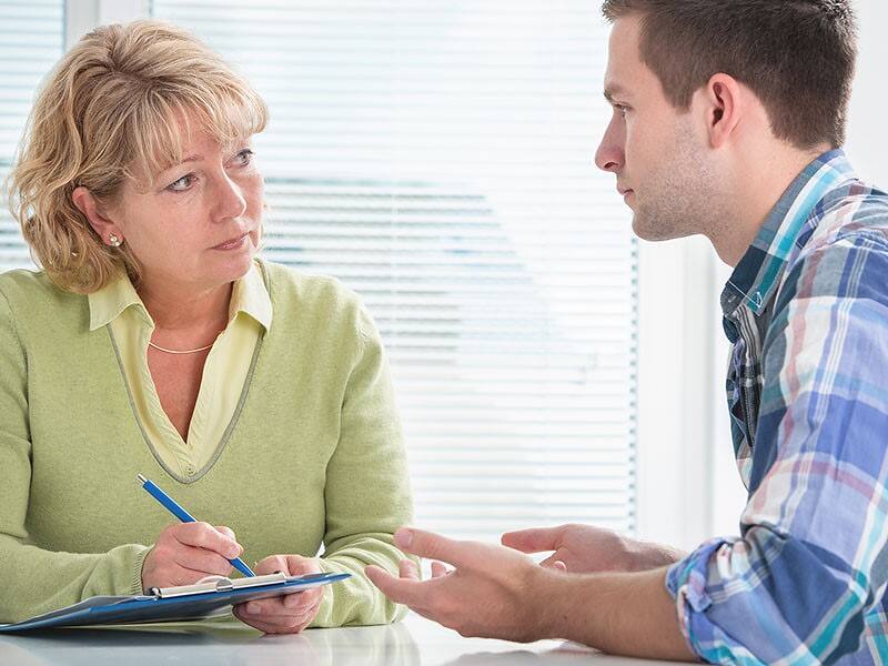 Counselor taking notes while listening attentively to a male patient, discussing treatment options for rapid opiate detox