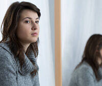 Young woman in gray sweater with thoughtful expression, looking away from mirror reflection