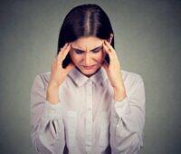 Woman in white shirt holding her head, appearing to have a headache or experiencing stress