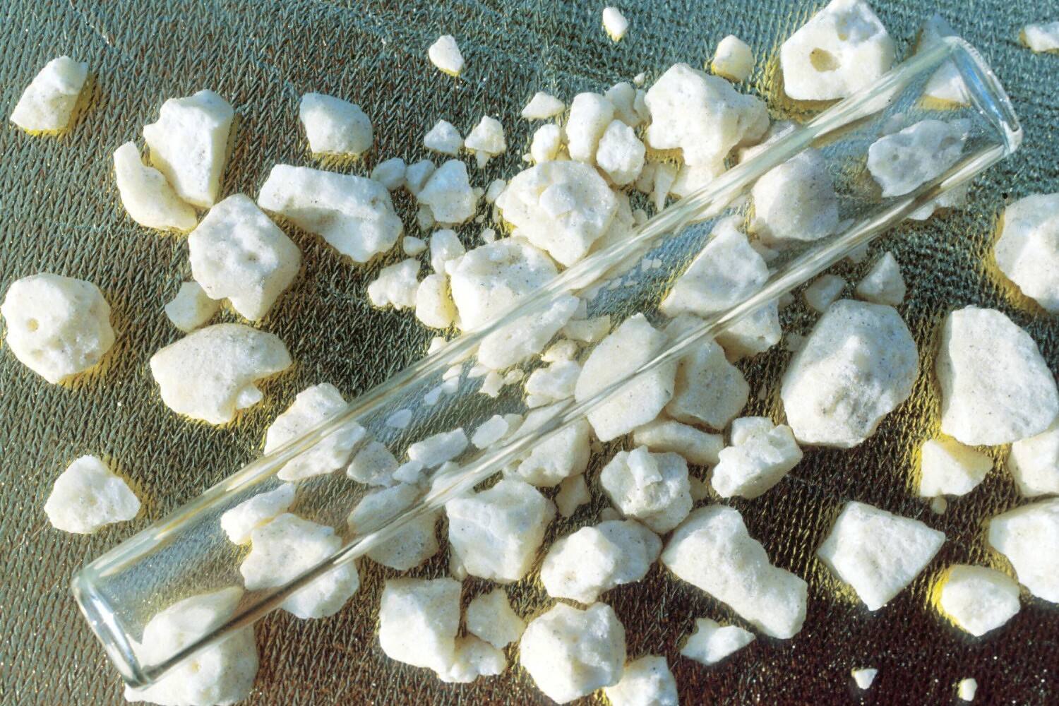 Close-up of crack cocaine rocks scattered on a textured surface with glass tubes, illustrating the appearance and paraphernalia associated with crack cocaine use