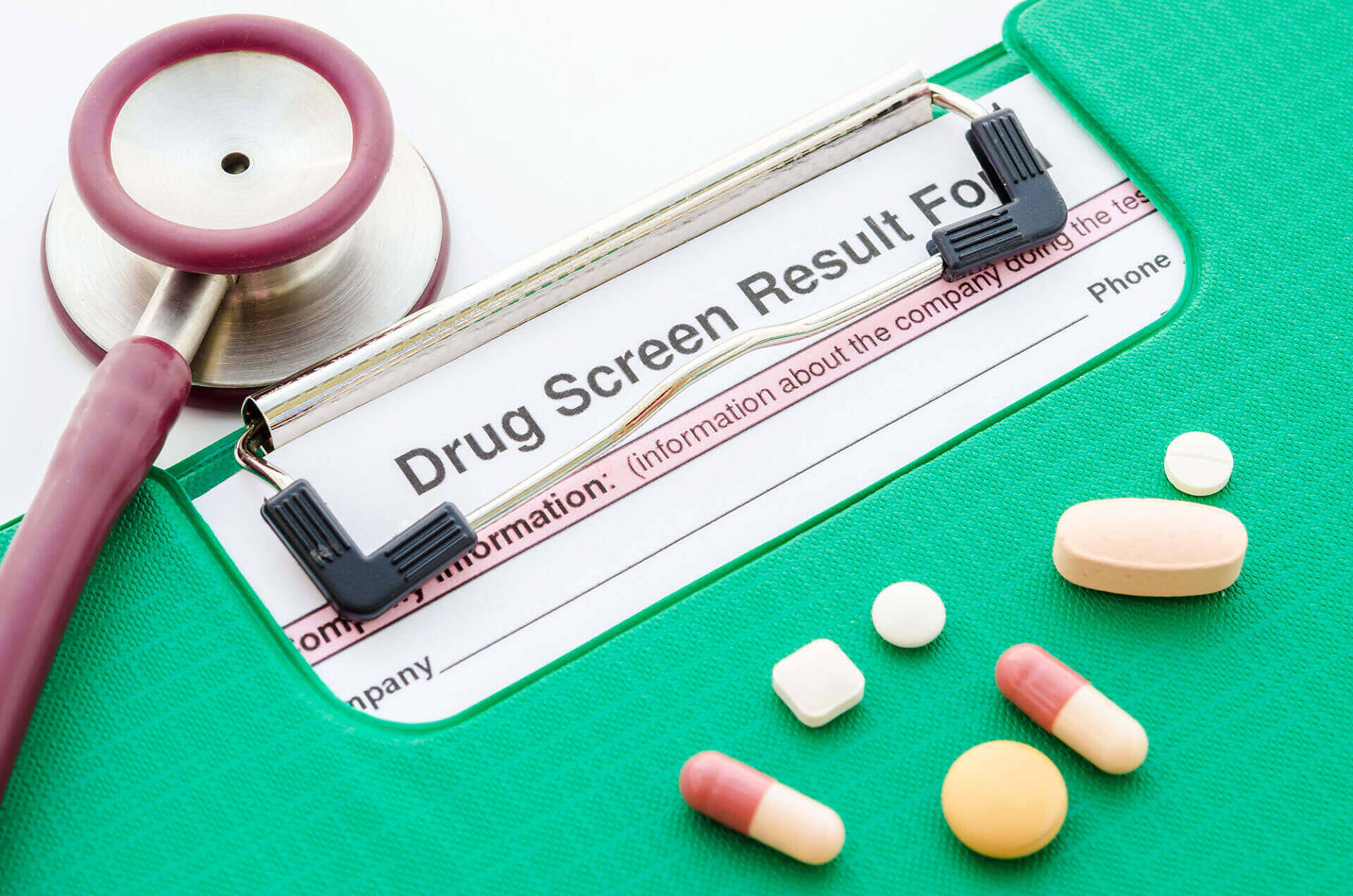 Medical clipboard with "Drug Screen Result Form" visible, alongside a stethoscope and various pills, illustrating the process of drug testing and substance abuse evaluation