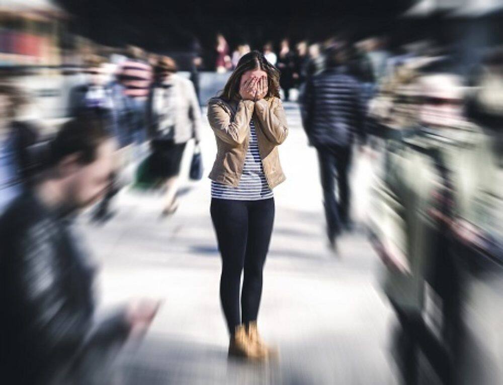 Woman covering face in distress, surrounded by blurred crowd, depicting anxiety and isolation associated with opiate addiction
