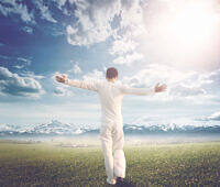 Man in white clothing with arms outstretched, facing mountains and bright sky, symbolizing freedom and recovery after rapid opiate detox