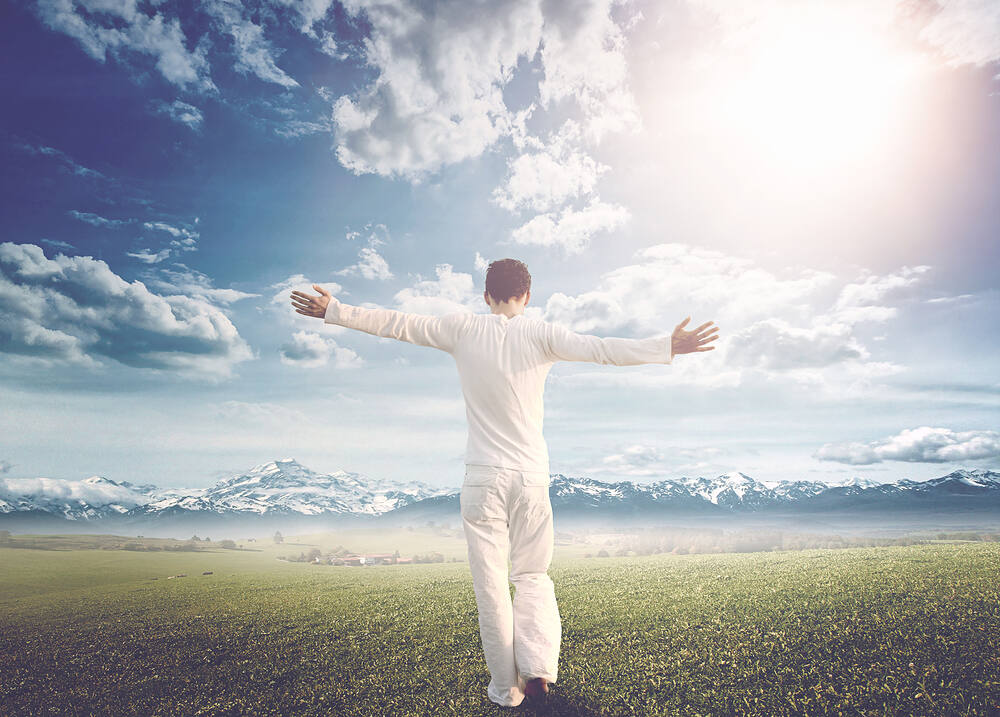 Man in white clothing with arms outstretched, facing mountains and bright sky, symbolizing freedom and recovery after rapid opiate detox