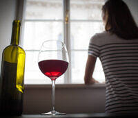 Woman looking out window with wine bottle and glass in foreground, depicting alcohol addiction and isolation