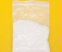 A clear plastic bag containing white powder, commonly associated with mephedrone, on a yellow background, highlighting its appearance for educational purposes in drug awareness.