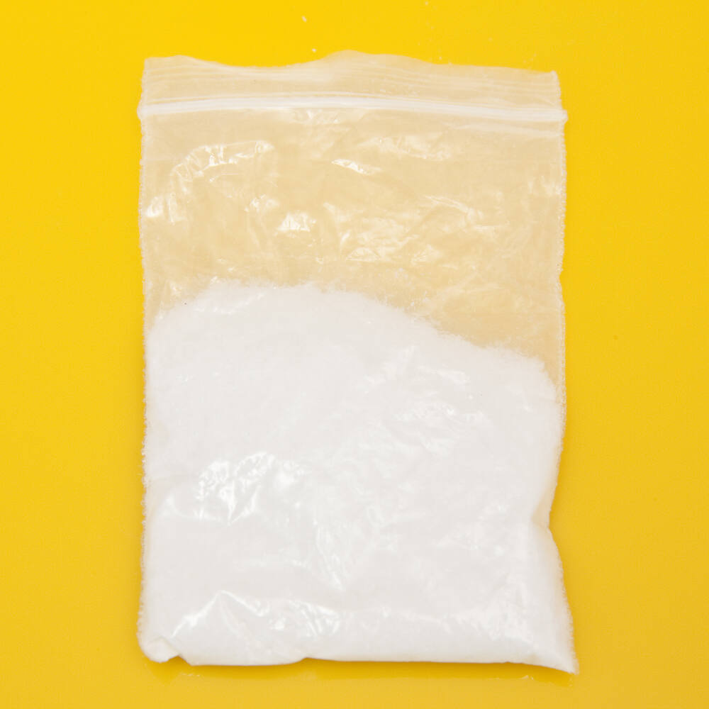 A clear plastic bag containing white powder, commonly associated with mephedrone, on a yellow background, highlighting its appearance for educational purposes in drug awareness.