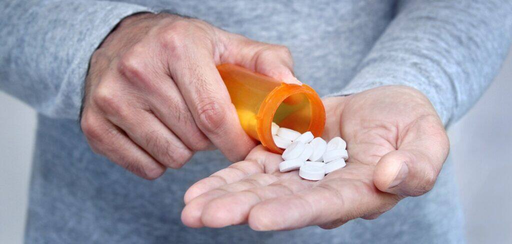 Person pouring white pills from orange prescription bottle into their palm