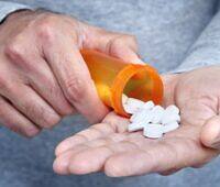 Person pouring white pills from orange prescription bottle into their palm