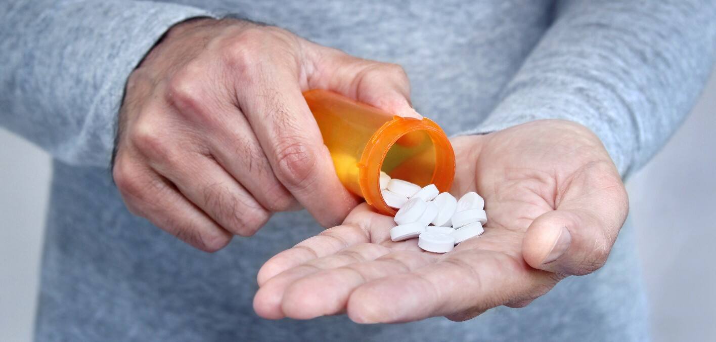 Person pouring white pills from orange prescription bottle into their palm