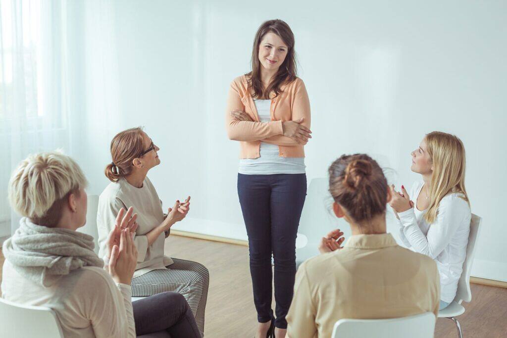 Female counselor leading a group therapy session with four participants in a bright, supportive environment