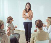 Female counselor leading a group therapy session with four participants in a bright, supportive environment