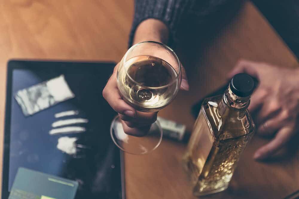 Lines of cocaine powder next to a glass of alcoholic drink on a reflective surface, illustrating the hazardous combination of cocaine and alcohol use