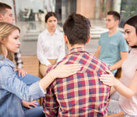 Young adults participating in a supportive group therapy session for substance abuse recovery, sitting in a circle with comforting gestures