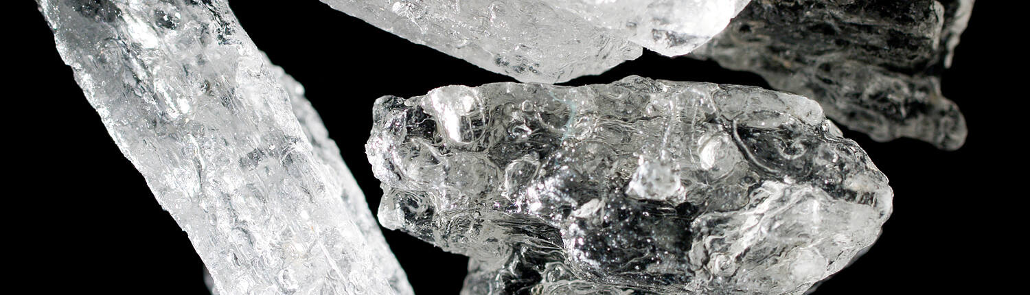 Macro photograph of crystal meth shards showing translucent, jagged crystalline structures against a black background