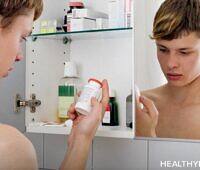 Shirtless teenage boy looking at prescription medication bottle in bathroom medicine cabinet mirror