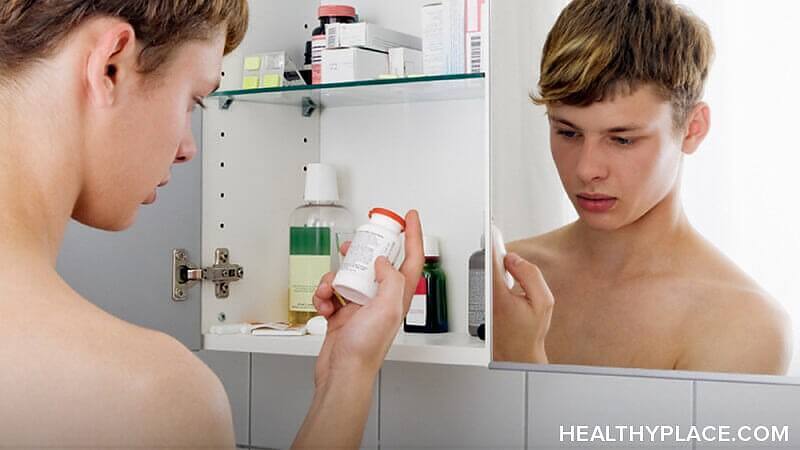 Shirtless teenage boy looking at prescription medication bottle in bathroom medicine cabinet mirror