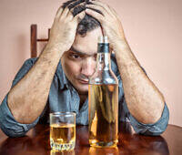 Distressed man holding his head with bottle and glass of alcohol on table, depicting alcohol addiction and anxiety