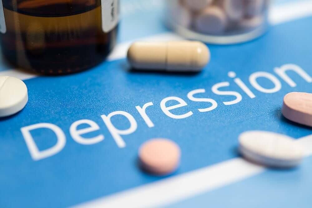 The word 'Depression' printed on a blue background surrounded by various antidepressant pills and medication bottles