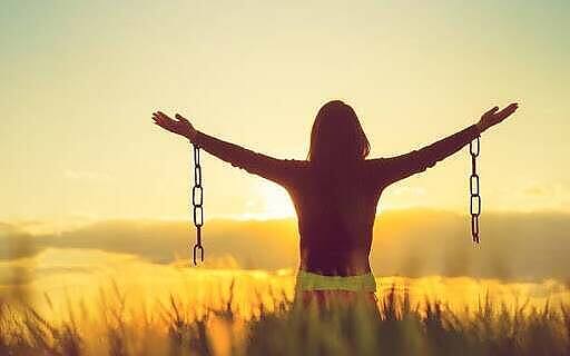 Silhouette of person with arms raised breaking chains at sunset in a field, symbolizing freedom from alcohol addiction during Christmas