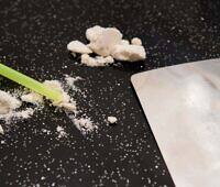 Close-up of crack cocaine rocks, powdered residue, green straw, and metal card on black background