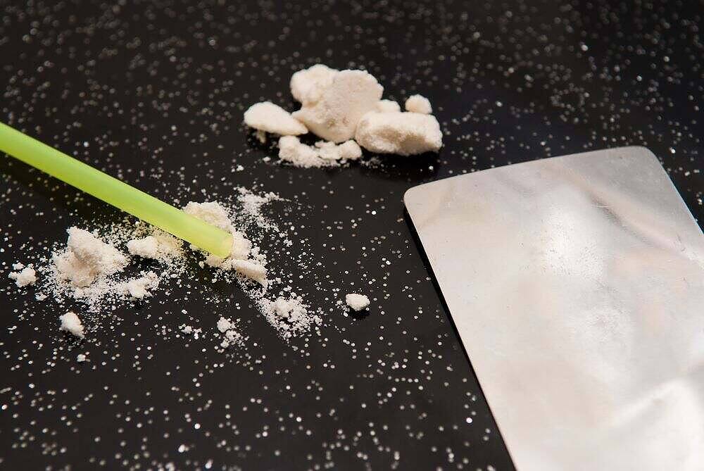 Close-up of crack cocaine rocks, powdered residue, green straw, and metal card on black background