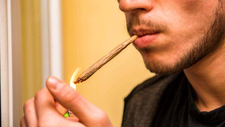 Close-up of a man lighting a marijuana joint, illustrating the act of drug use and potential addiction