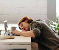 Woman in wheelchair sleeping at desk with laptop, showing signs of extreme fatigue possibly related to substance use